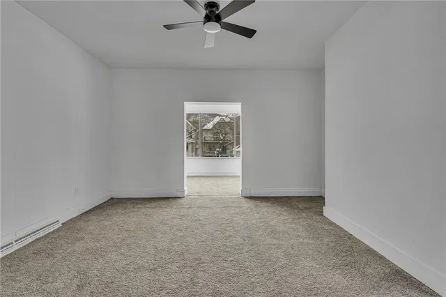 an empty room with kitchen view and a ceiling fan