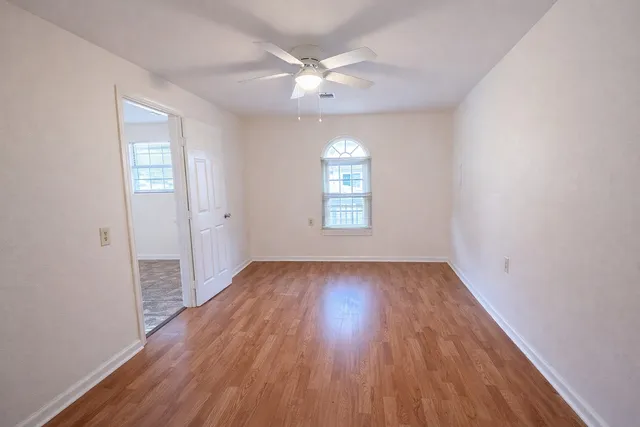 an empty room with wooden floor chandelier fan and windows