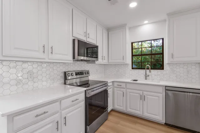 a kitchen with white cabinets appliances a sink and a window