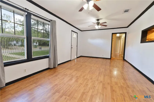an empty room with wooden floor chandelier fan and windows