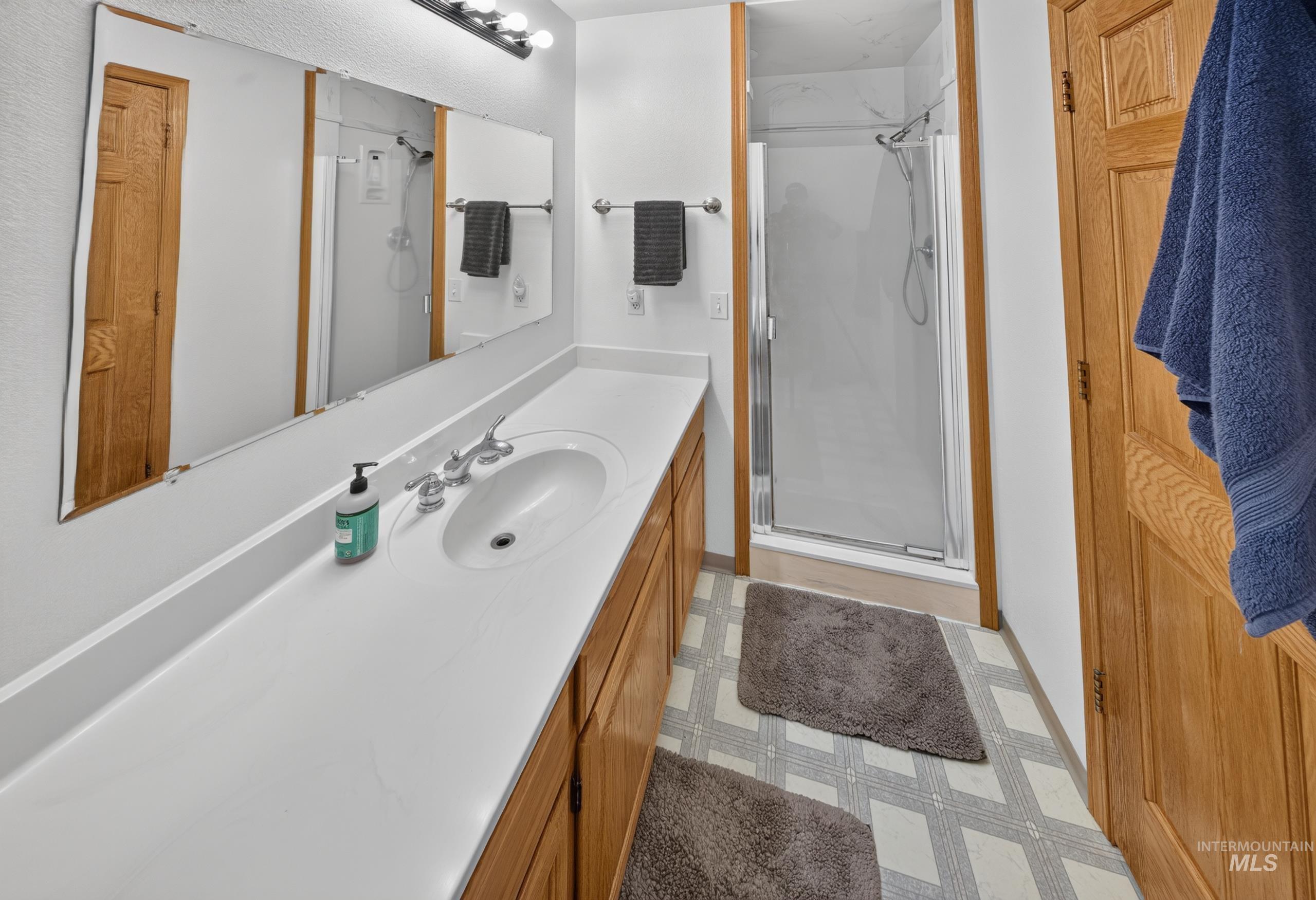 5540 Finley Road Fruitland, ID 83619 - Photo 38 of 50 Recessed single-basin sink with chrome-finish faucet, elongated vanity with light-tone countertop, wood-finish cabinetry, and glass-enclosed shower