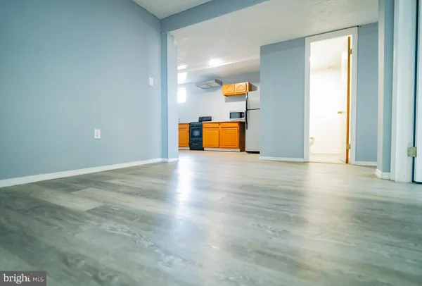 an empty room with wooden floor and way to kitchen