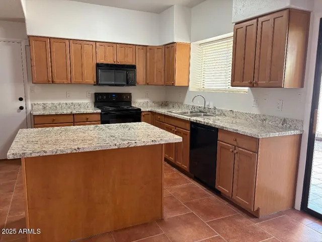 a kitchen with granite countertop a sink a stove top oven a refrigerator and cabinets