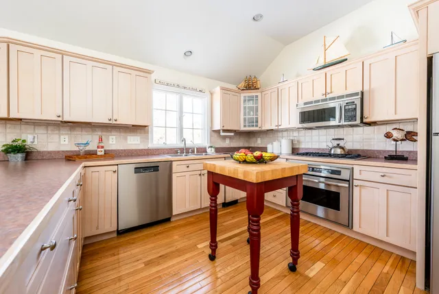 a kitchen with stainless steel appliances granite countertop a stove top oven a sink dishwasher and white cabinets with wooden floor