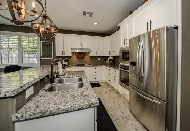 a kitchen with stainless steel appliances granite countertop a stove a sink a refrigerator and a dining table with wooden floor