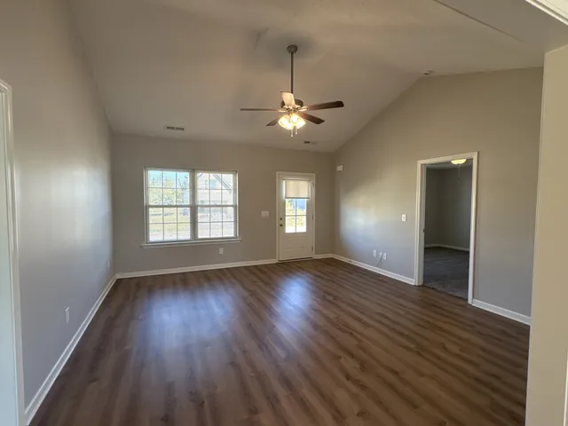 an empty room with wooden floor chandelier fan and windows