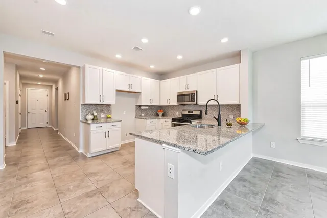 a kitchen with stainless steel appliances granite countertop a stove top oven a sink a refrigerator and white cabinets