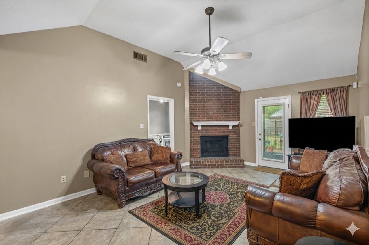 7788 Reese Road Memphis, TN 38133 - Photo 4 of 23 Spacious living area featuring a vaulted ceiling with a ceiling fan, a brick fireplace with a white mantel, and neutral-toned wall paint