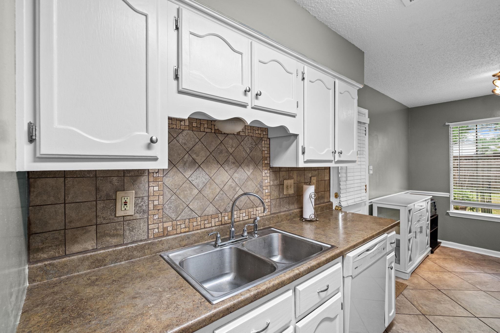7788 Reese Road Memphis, TN 38133 - Photo 5 of 23 Kitchen featuring white cabinetry, a double basin stainless steel sink, a tiled backsplash with mosaic accents, and a window with blinds