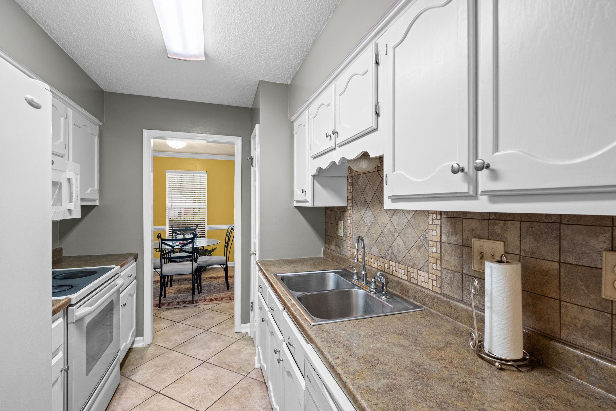 7788 Reese Road Memphis, TN 38133 - Photo 7 of 23 Galley kitchen featuring white cabinetry, a double basin stainless steel sink, laminate countertops, and a tiled backsplash