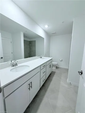 a spacious bathroom with a double vanity sink a mirror and a toilet