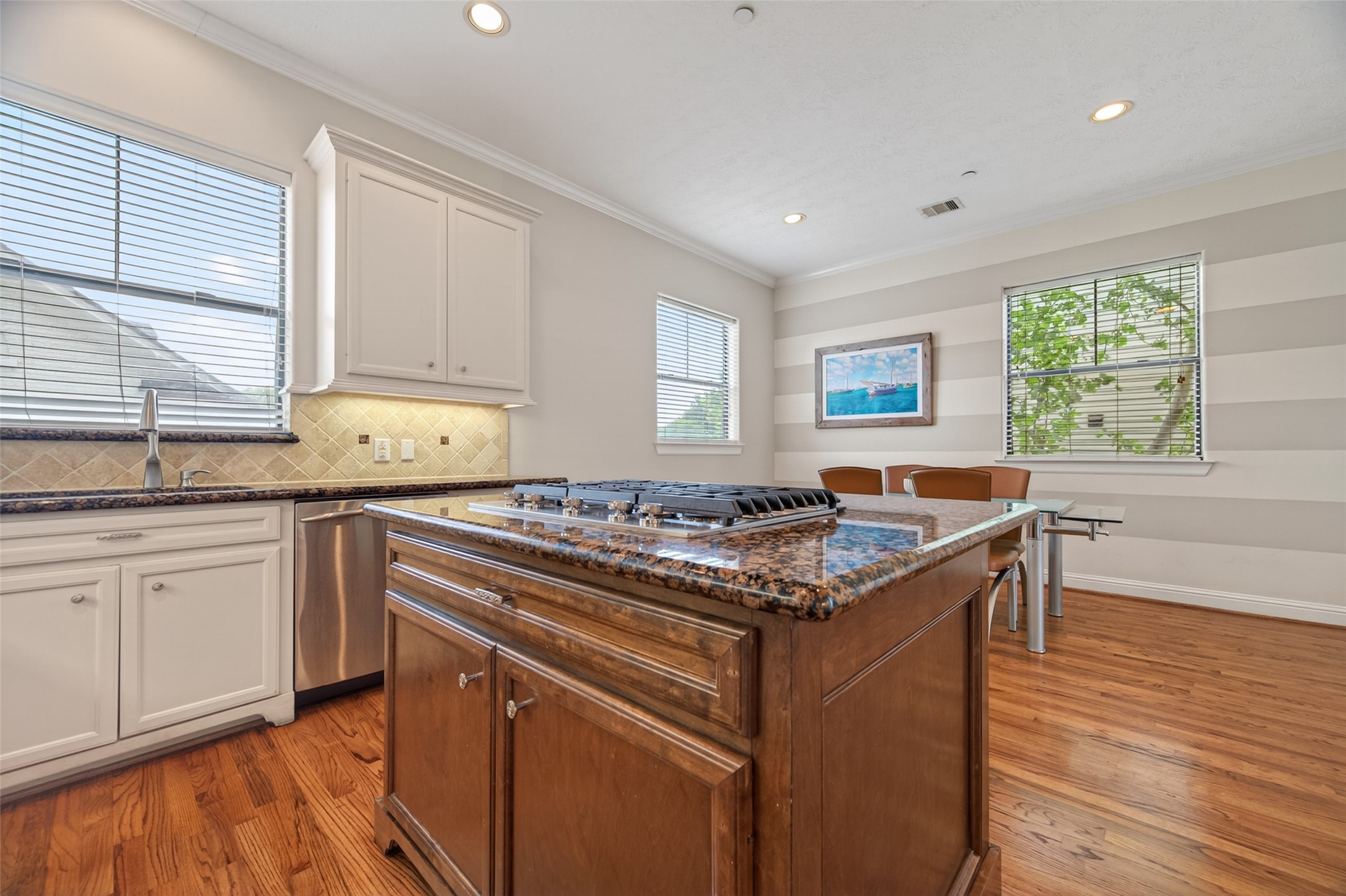 2611 Riverside Drive, Unit C Houston, TX 77004 - Photo 16 of 50 This bright kitchen features hardwood floors, a large granite island with a built-in cooktop, white cabinetry, and stainless steel appliances. It opens to a dining area with natural light from multiple windows.