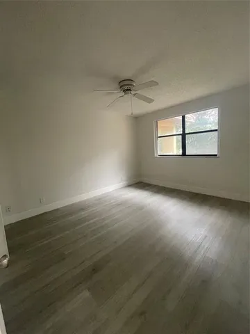an empty room with wooden floor chandelier fan and windows