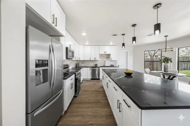 a kitchen with stainless steel appliances granite countertop a sink a stove a refrigerator and island with wooden floor