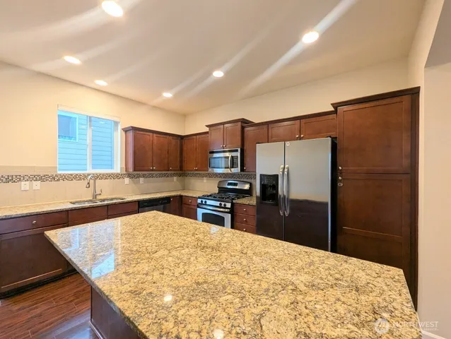 a kitchen with stainless steel appliances kitchen island granite countertop a refrigerator and a sink