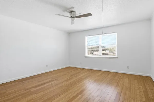 an empty room with wooden floor ceiling fan and windows