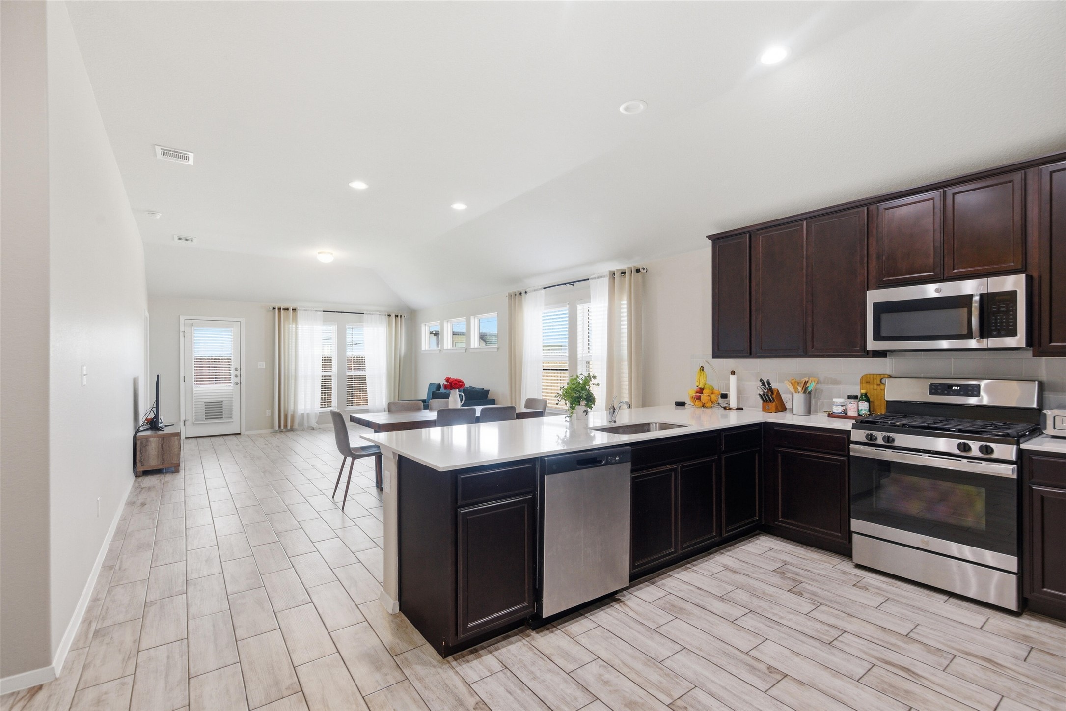 269 Gaida Loop Georgetown, TX 78628 - Photo 4 of 20 Kitchen with stainless steel appliances, lofted ceiling, wood tiled floors, dark wood finish cabinets, and a peninsula