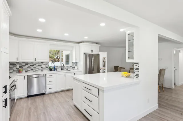 a kitchen that has a lot of white cabinets and stainless steel appliances