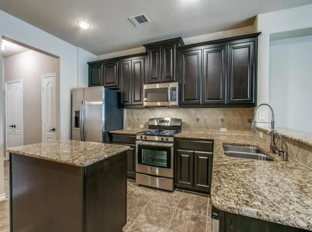 a kitchen with stainless steel appliances granite countertop wooden cabinets a stove and a sink