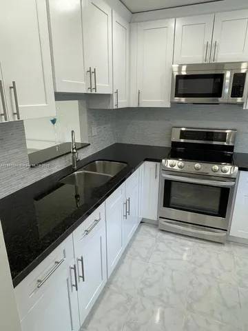 a kitchen with granite countertop a stove a microwave a sink and cabinets