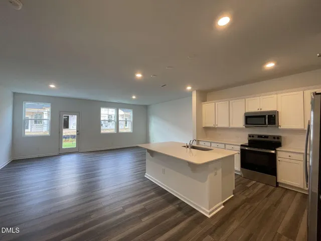 a kitchen with stainless steel appliances granite countertop a stove top oven a sink dishwasher and a refrigerator with wooden floor