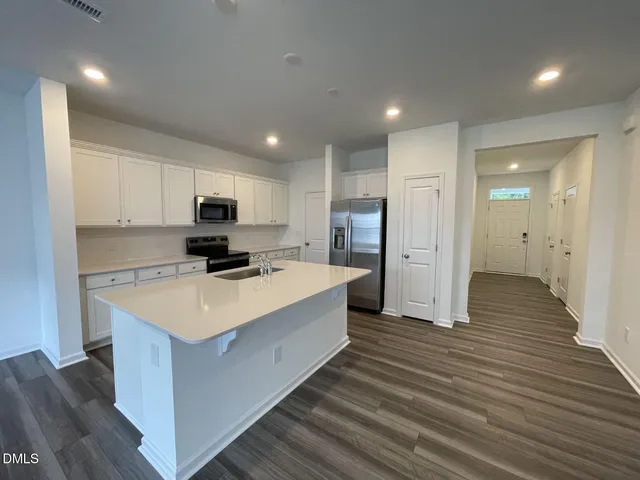 a large kitchen with stainless steel appliances a refrigerator oven a sink dishwasher and a dining table with wooden floor