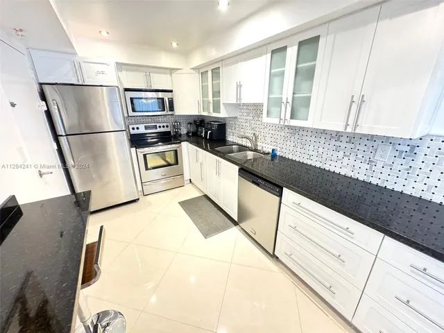 a kitchen with granite countertop a refrigerator a sink and white cabinets