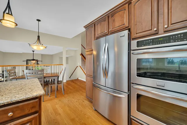 a kitchen with stainless steel appliances granite countertop a refrigerator a stove a dining table and chairs with wooden floor