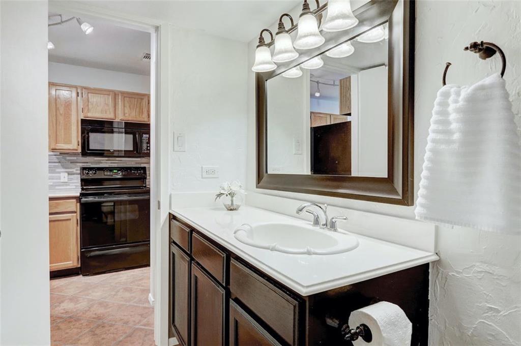 3115 Helms Street, Unit 204 Austin, TX 78705 - Photo 7 of 13 A well-lit bathroom vanity with a clean white countertop offers convenience adjacent to a functional kitchen.