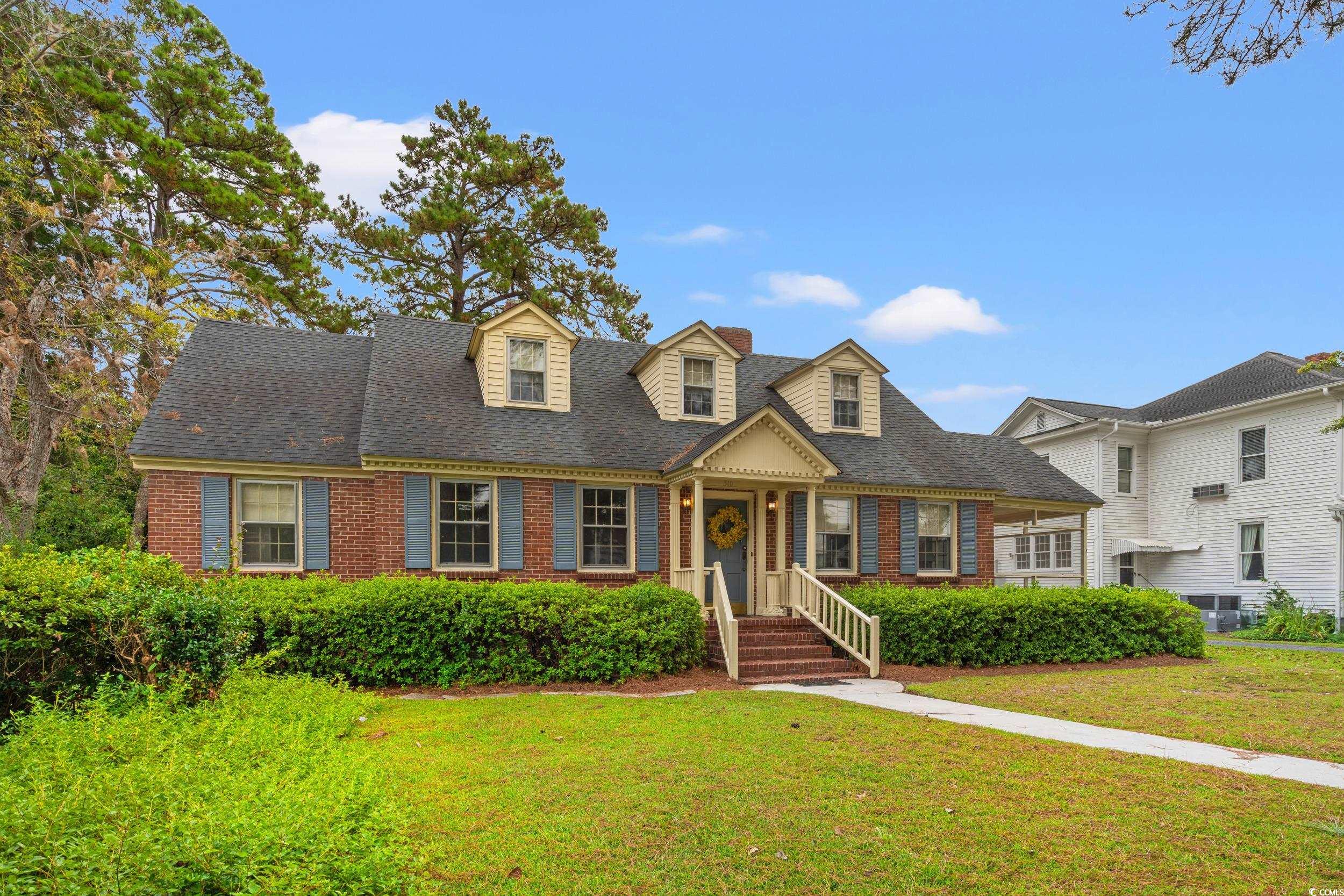 310 North Main Street Mullins, SC 29574 - Photo 10 of 35 Cape cod-style house featuring a front yard, brick siding, covered porch, and a shingled roof