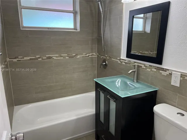 a bathroom with a granite countertop sink a toilet a mirror and bathtub