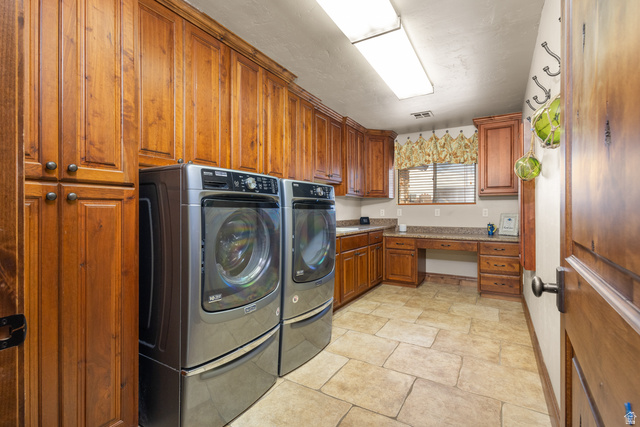 892 Cambridge Drive St. George, UT 84770 - Photo 37 of 65 Laundry room featuring extensive wood cabinetry, stone-look tile flooring, built-in desk, and counter space