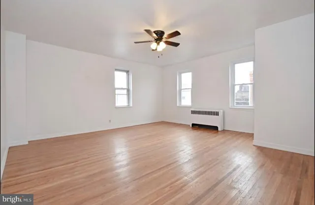 an empty room with wooden floor ceiling fan and windows