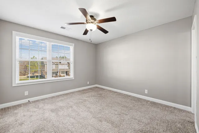 an empty room with ceiling fan and windows