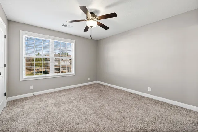 an empty room with ceiling fan and windows