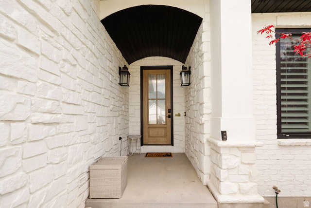 924 Country Lane Farmington, UT 84025 - Photo 6 of 91 Covered entry featuring a natural wood-finish door with glass panels, white stone veneer siding, and a dark arched soffit