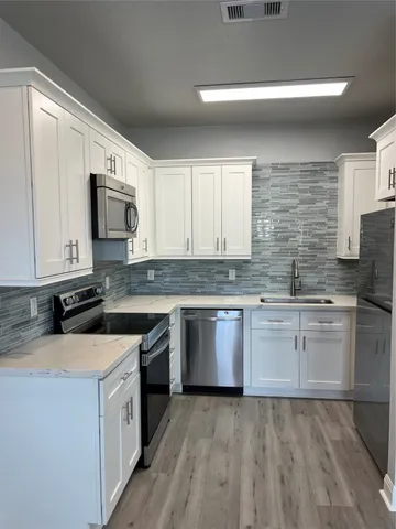 a kitchen with granite countertop a sink a stove top oven and white cabinets