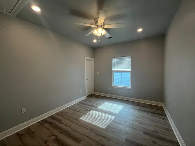 an empty room with wooden floor chandelier fan and windows