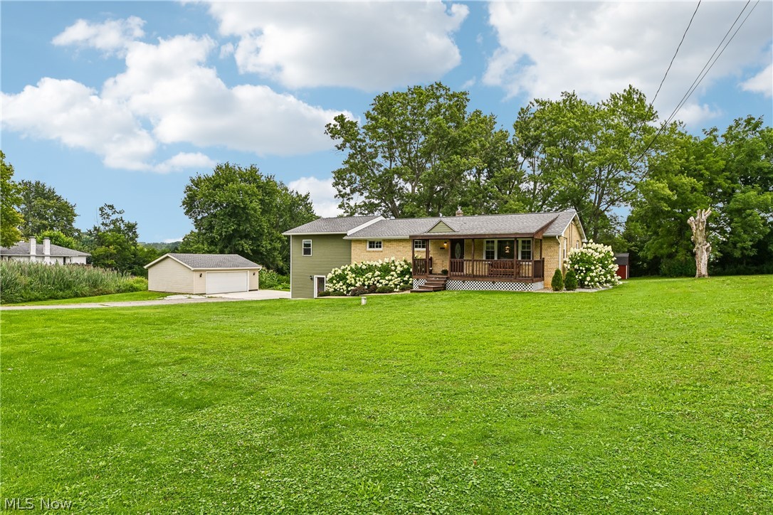 15111 Mt Eaton Road North Rittman, OH 44270 - Photo 6 of 50 Expansive green lawn, two-car detached garage, covered porch with railing, mature landscaping with flowering shrubs, and a multi-level exterior