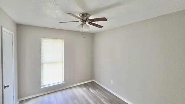 an empty room with wooden floor fan and windows