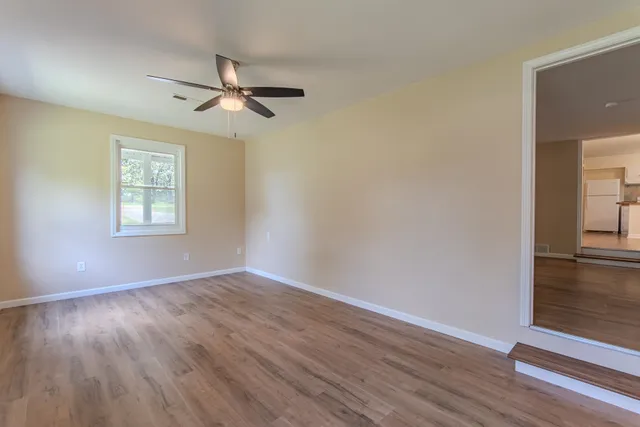 an empty room with wooden floor chandelier fan and windows