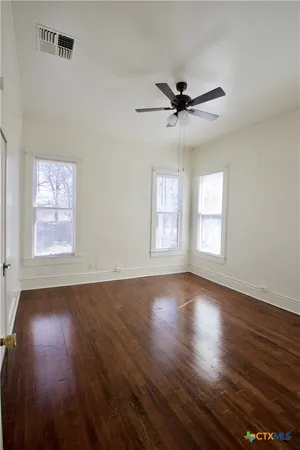 an empty room with wooden floor a ceiling fan and windows