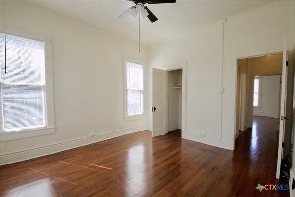 an empty room with wooden floor cabinet and windows