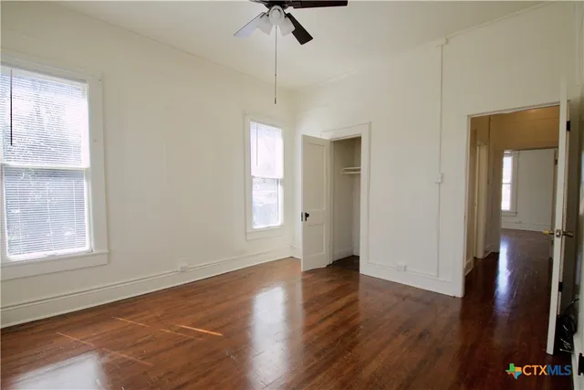 an empty room with wooden floor cabinet and windows
