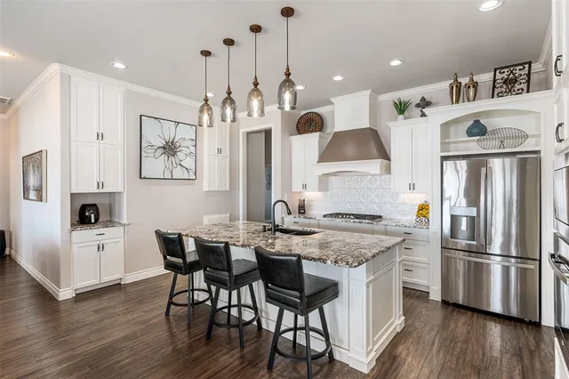a kitchen with stainless steel appliances granite countertop a stove a refrigerator a kitchen island a dining table and chairs with wooden floor