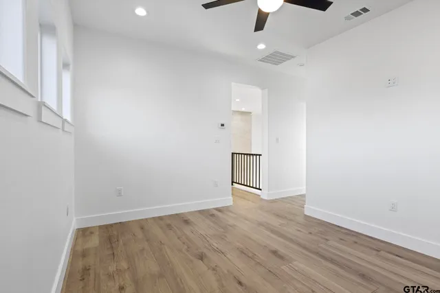 an empty room with wooden floor ceiling fan and window