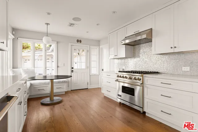 a large white kitchen with granite countertop a stove a sink a refrigerator and white cabinets with wooden floor