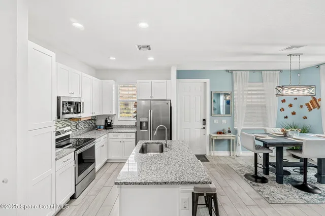 a kitchen with stainless steel appliances granite countertop a kitchen island a stove a refrigerator a sink a dining table and chairs