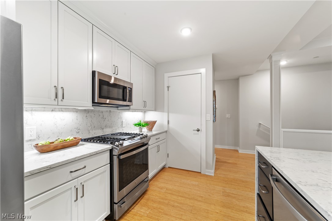 2044 Random Road, Unit 101 Cleveland, OH 44106 - Photo 15 of 44 Kitchen with appliances with stainless steel finishes, tasteful backsplash, light hardwood / wood-style floors, and white cabinetry