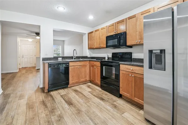 a kitchen with stainless steel appliances granite countertop a stove top oven a sink dishwasher and a refrigerator with wooden floor